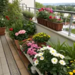 A small flower garden balcony features colorful potted roses, petunias, and daisies arranged along a beige wall, with terracotta and white planters placed on both the tiled floor and wooden boxes. The metal-railed space overlooks a tree-lined landscape.