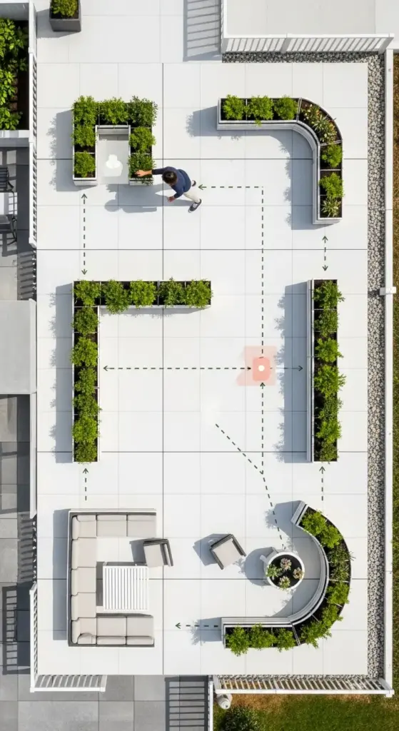 An overhead shot of a modern rooftop terrace with a clean, white-tiled floor. The space is segmented into seating areas using curved and straight planter boxes filled with lush green plants, which act as a natural privacy fence. A person is visible in the upper section, and the layout demonstrates creative "Privacy Fence Ideas" for urban outdoor spaces.