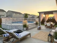 Coastal-inspired above ground pool with white wash wood deck, blue and white decor, and modern backyard pool landscaping