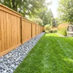 A beautiful wood privacy fence protected by a clean border of crushed landscaping rocks to prevent rot and trimmer damage.