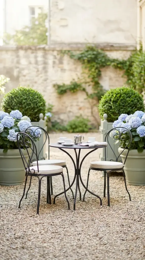 Parisian garden style backyard courtyard featuring a wrought iron bistro set, pea gravel, and oversized planters.