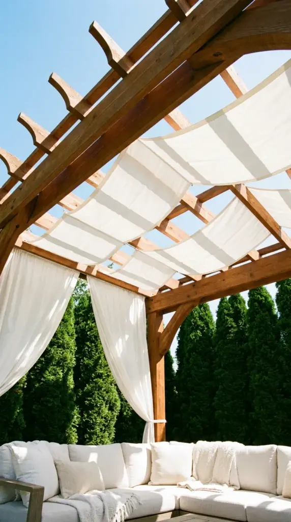 Classic wooden patio pergola featuring a white outdoor fabric canopy draped through the rafters for summer shade.