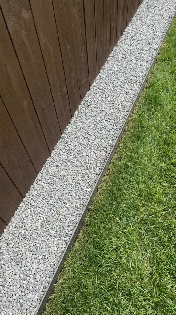 Clean pea gravel garden border with steel edging along a wood privacy fence.
