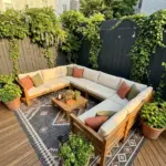 A beautifully styled small backyard patio featuring an oversized sectional, large outdoor rug, vertical garden, and dark painted fence to maximize space.